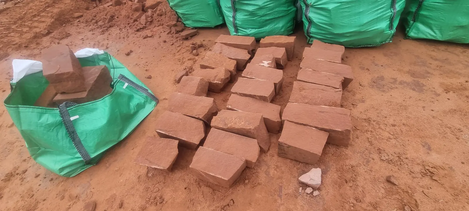 Pieces of red sandstone rough block laid out beside green bulk bags