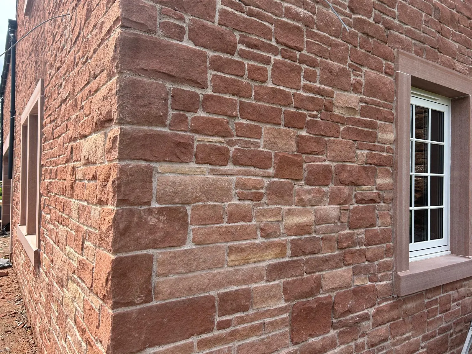 Corner of a red sandstone house showing quoins and a dressed window surround