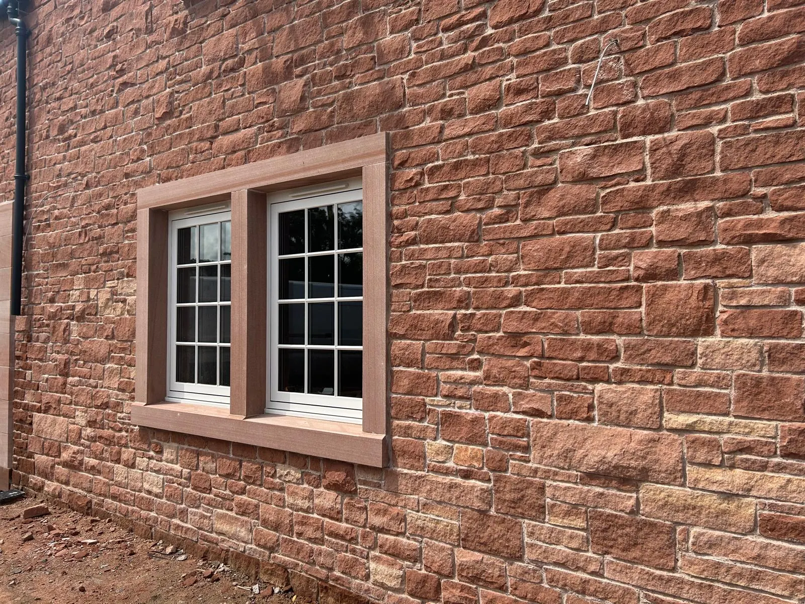 A finished house elevation in red sandstone with paired white sash windows and dressed surrounds